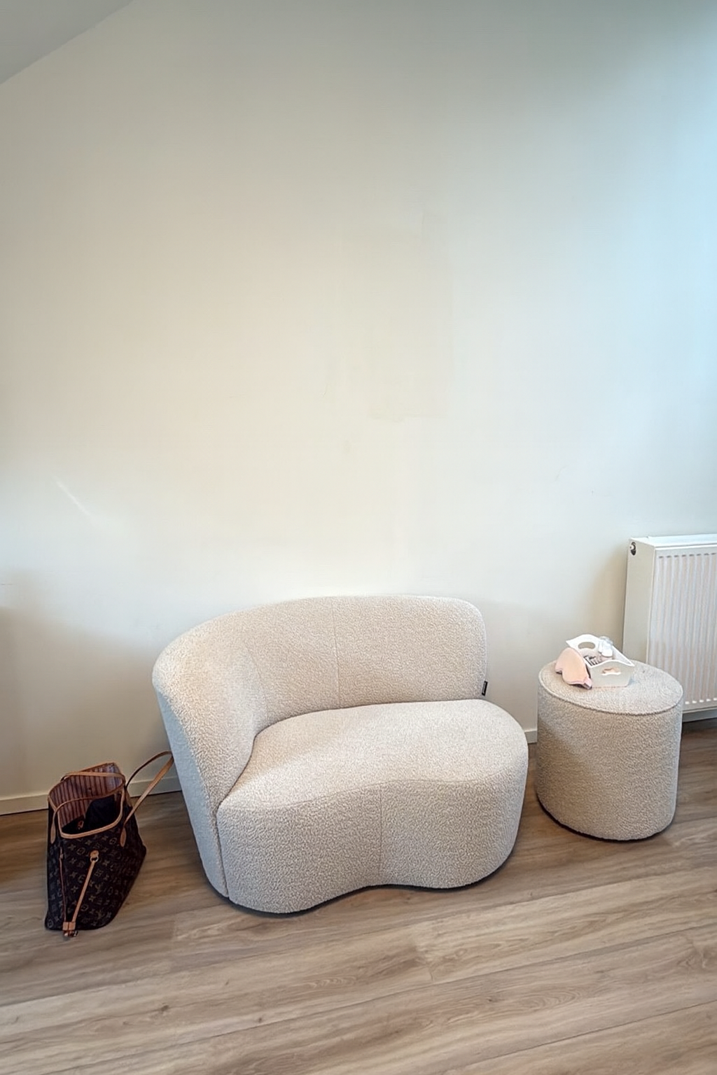 Een crèmekleurige bouclé fauteuil met bijzettafel in een lichte hoek van de studio